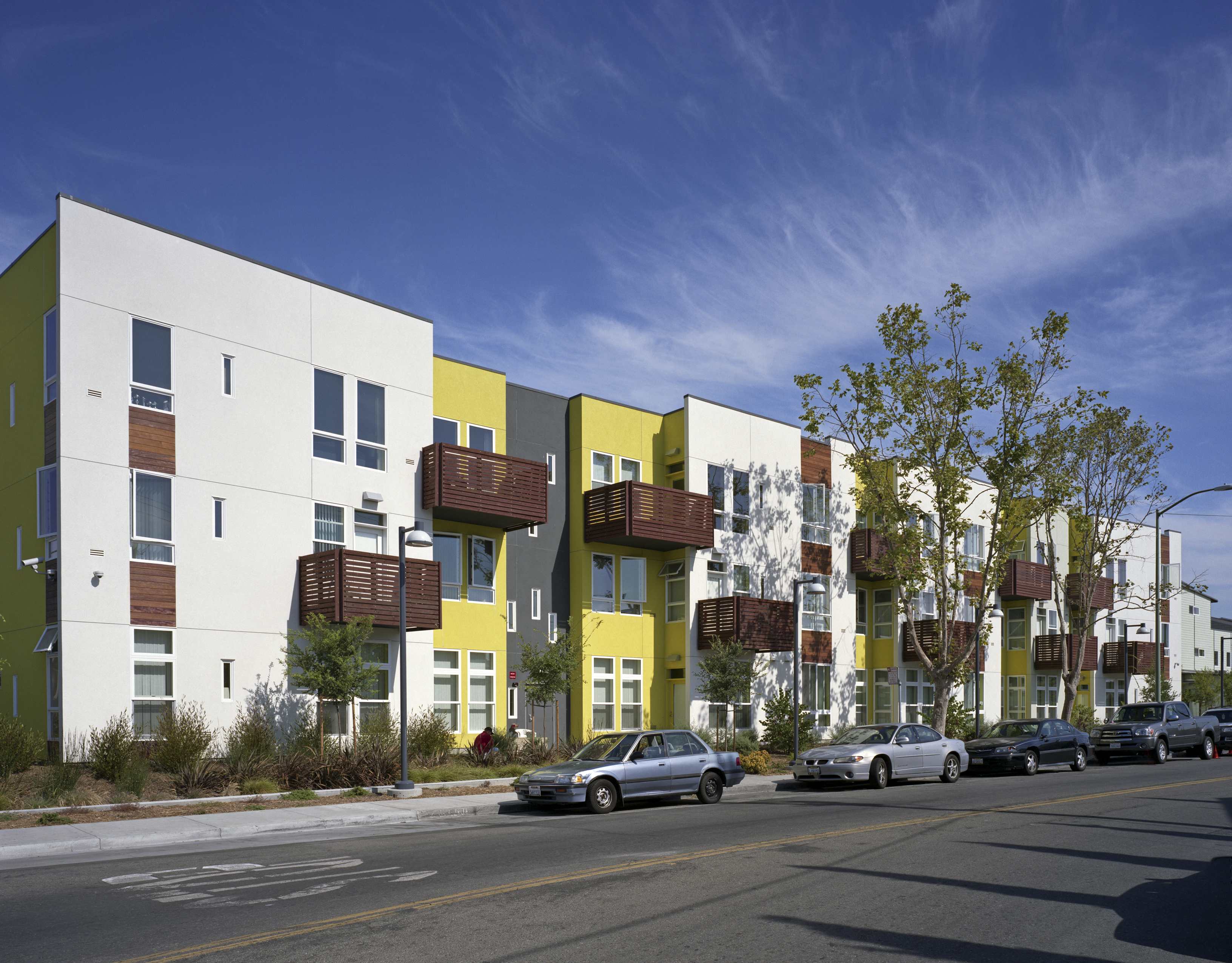 Elevation with wood-slat balconies and a planted sidewalk at Tassafaronga Village in East Oakland, CA. 