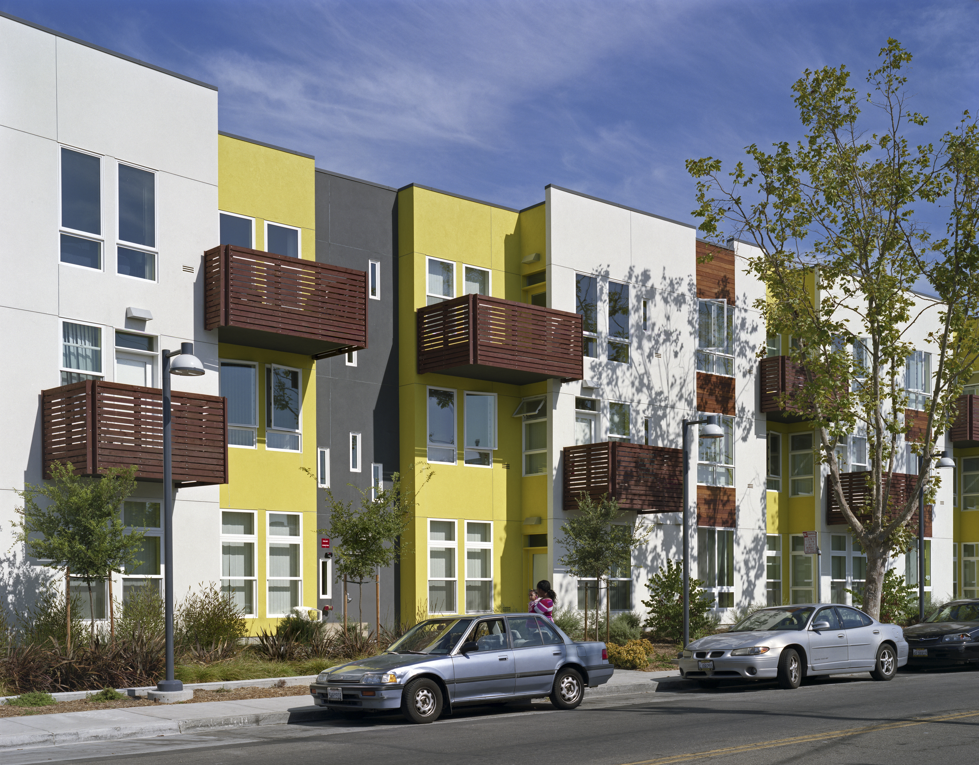 Elevation of apartment building with wood-slat balconies and a planted sidewalk at Tassafaronga Village in East Oakland, CA. 