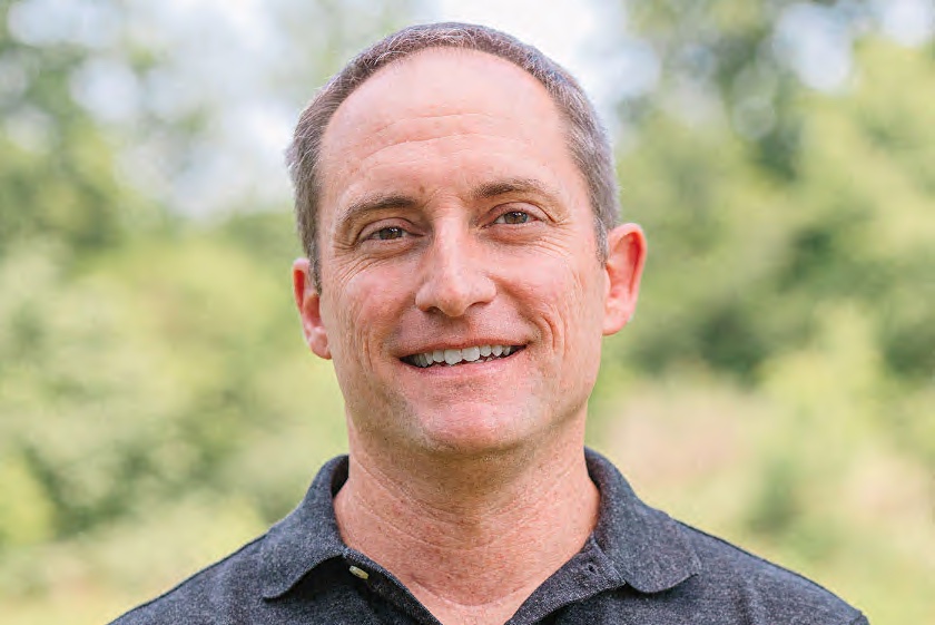 Headshot of a white man in a gray polo shirt photographed outdoors