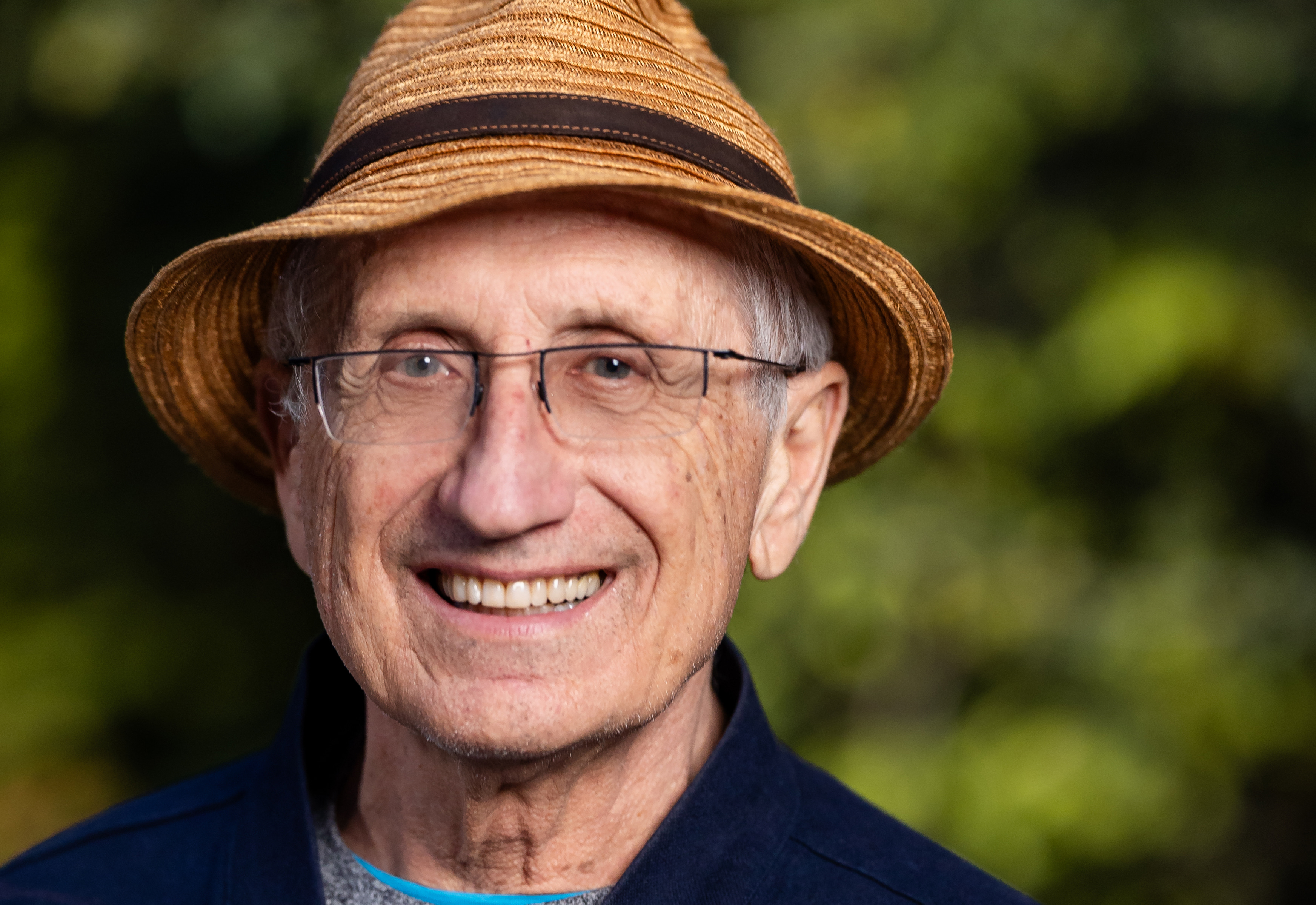 Headshot of man wearing rimless glasses and wearing straw hat