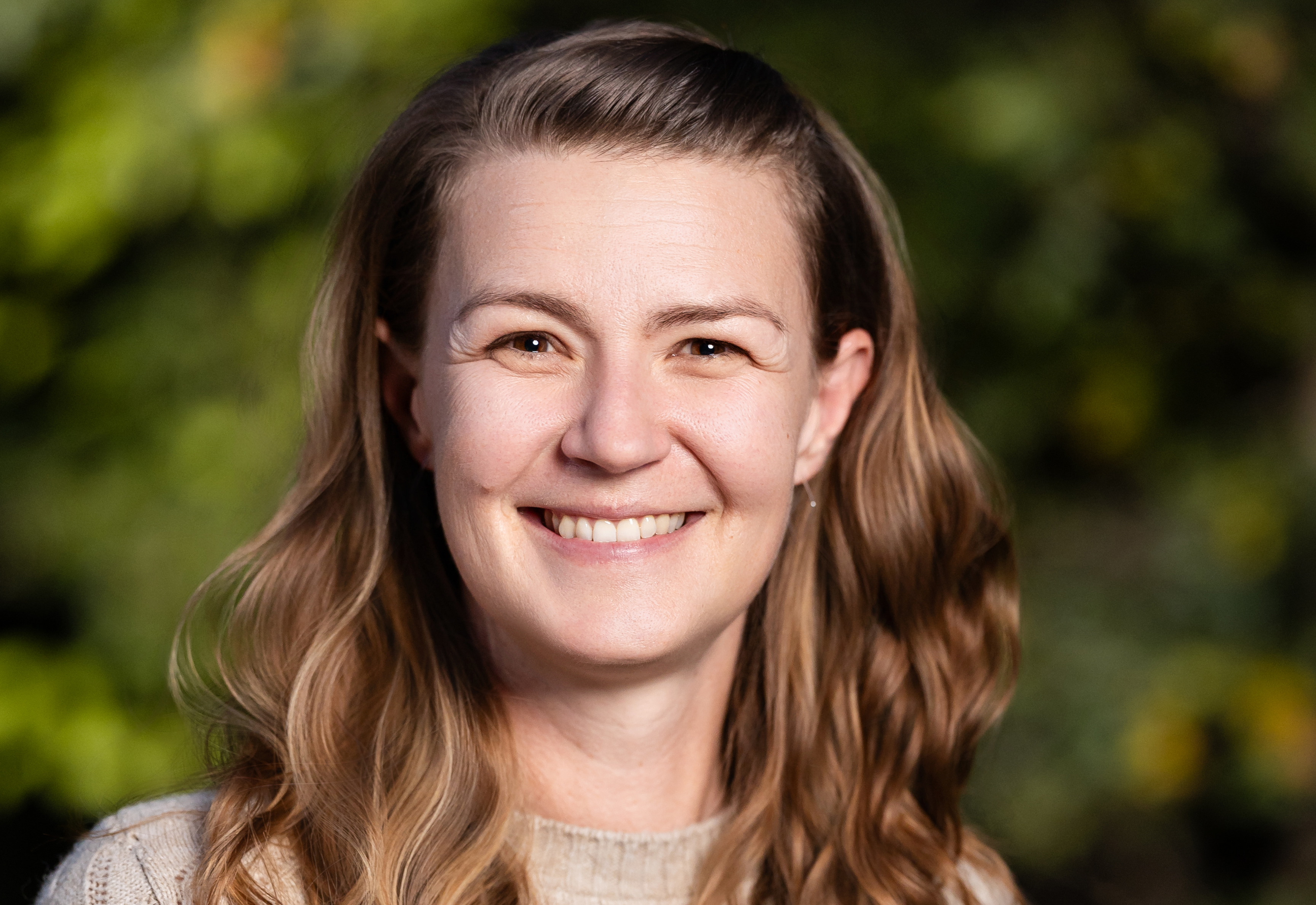 Headshot of woman with long, wavy light brown hair wearing beige sweater