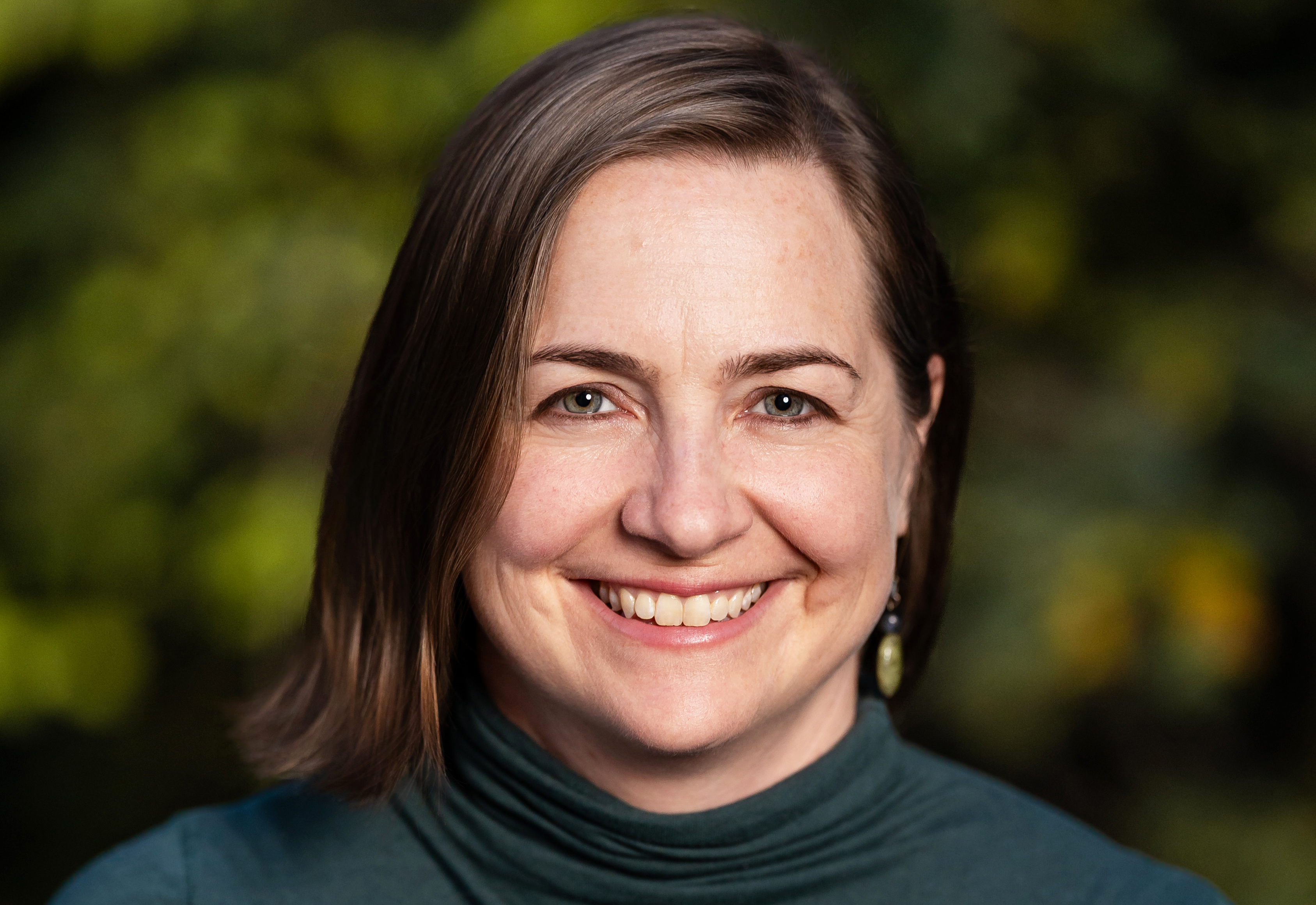 Headshot of woman with straight light brown hair wearing green turtleneck