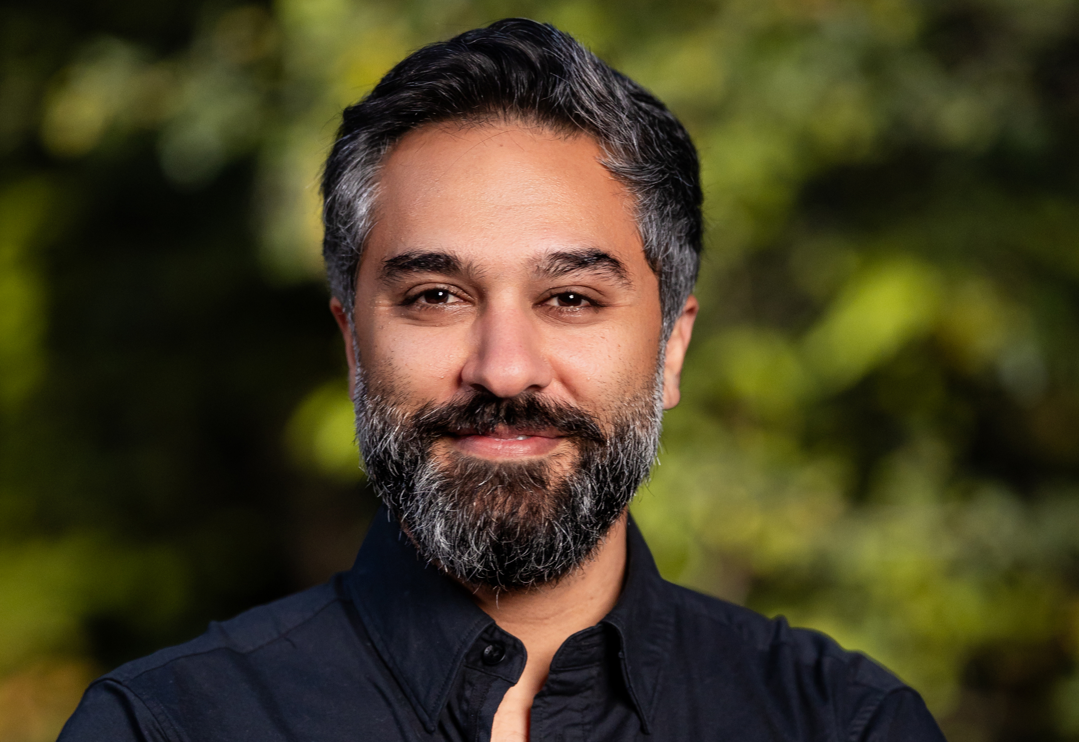 Man with black hair and beard with some gray wearing black collared shirt