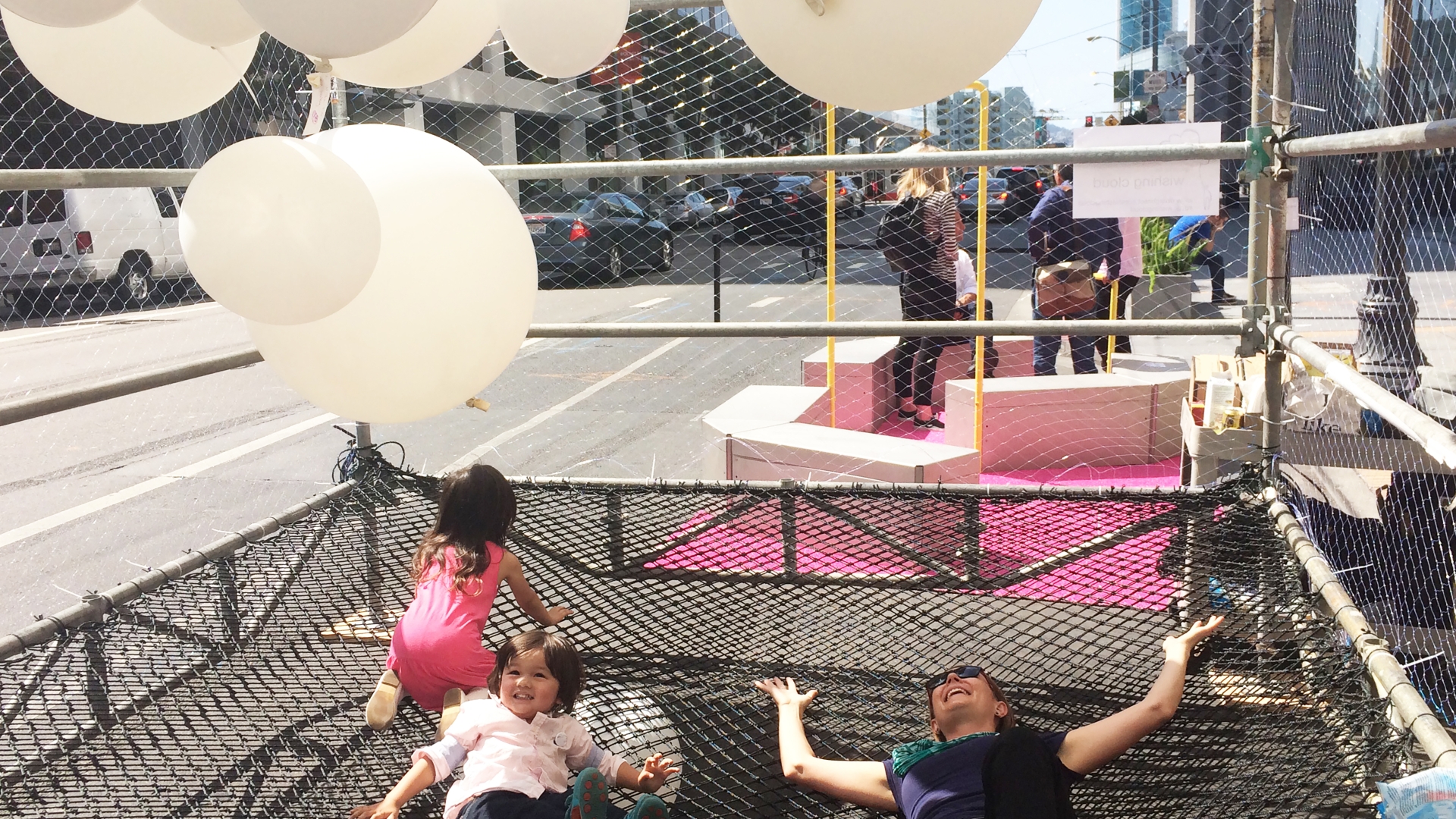 Woman and two children laying down in the net Wishing Cloud enclosure looking at the balloons.