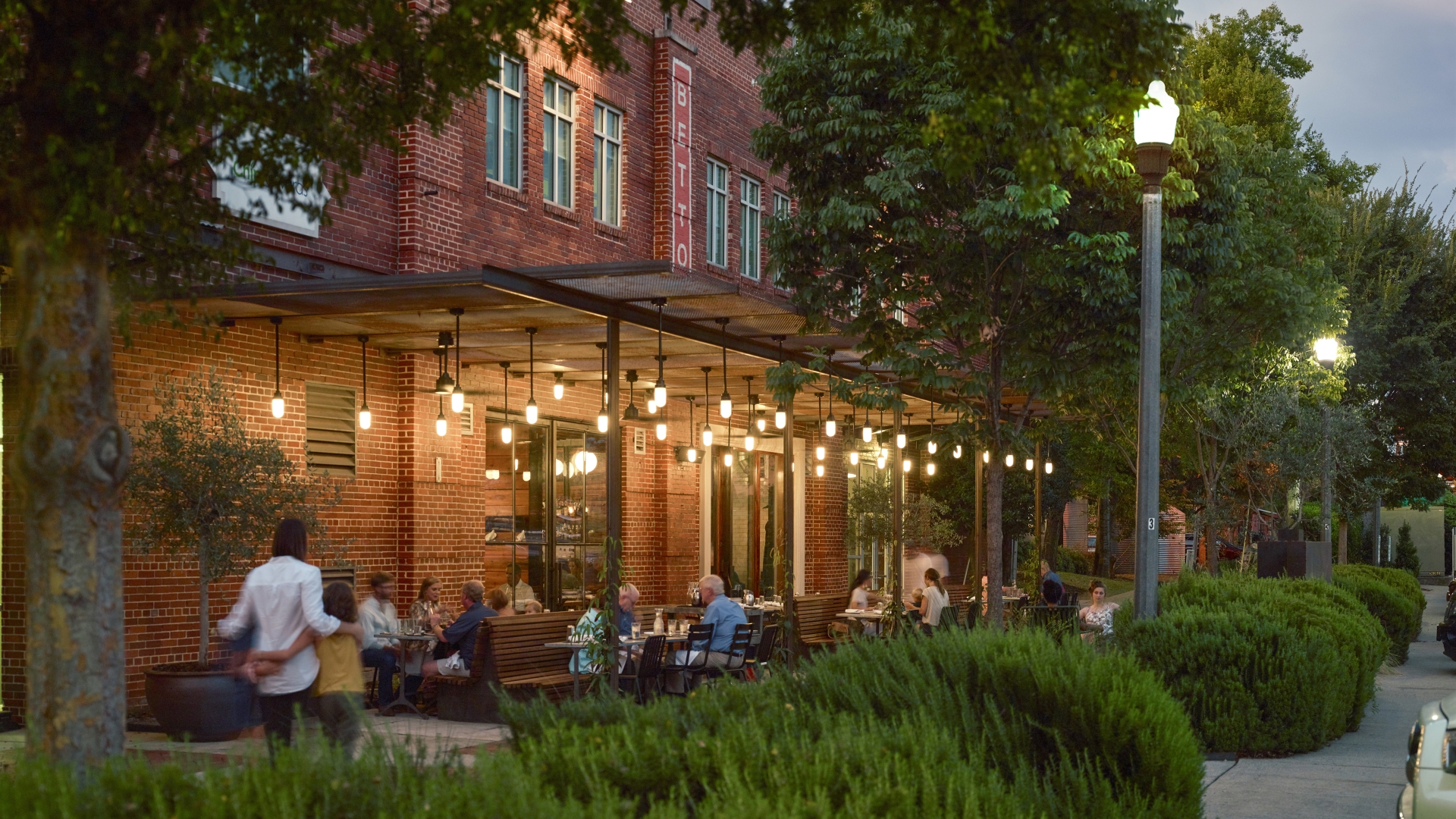 View from the southwest of people sitting at tables at Bettola Patio underneath the trellis at dusk in Birmingham, Alabama.