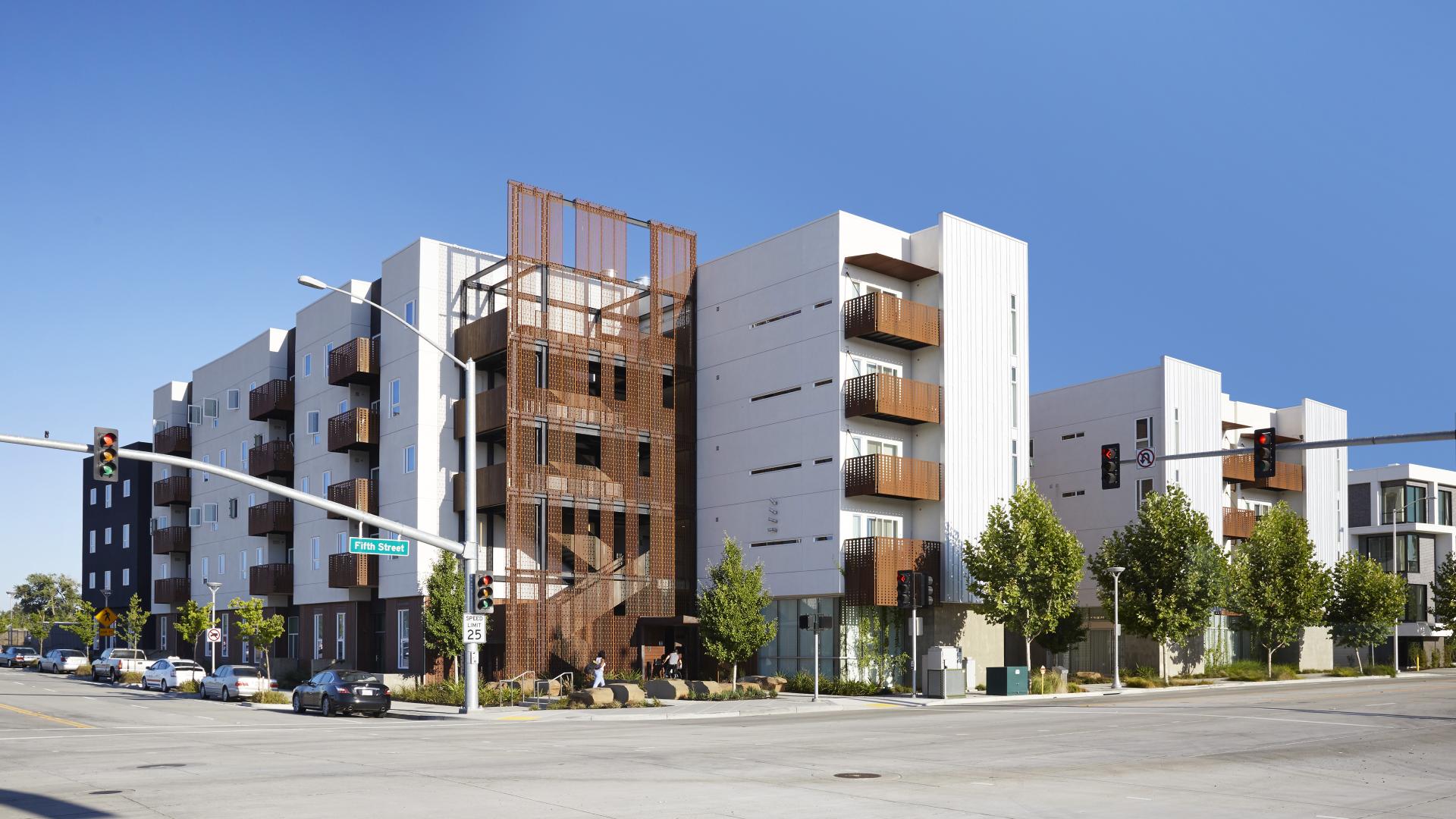 View of the Rivermark affordable apartment building from across a broad street, with a clear blue sky.