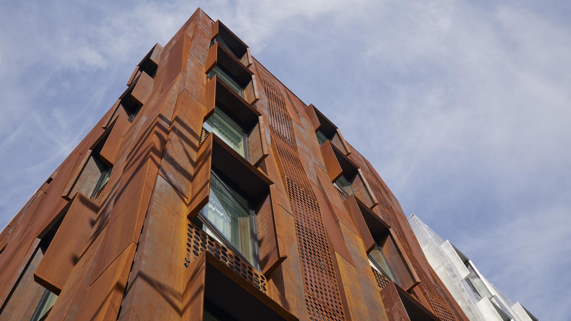 Detail of weathering steel rainscreen at corner, with clouded blue sky.