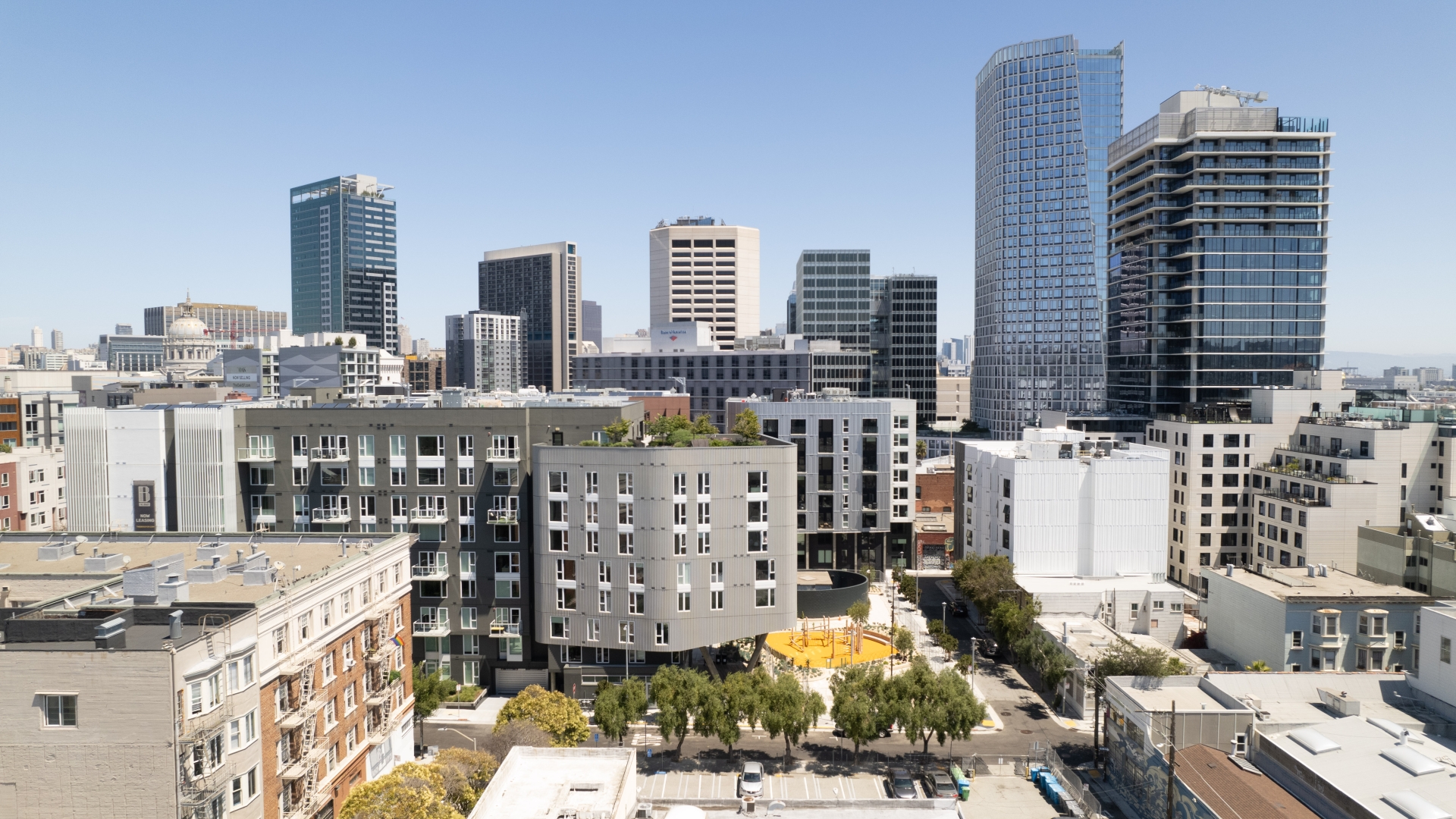 Aerial view of diverse buildings centered around a landscaped urban park with blue sky in background.