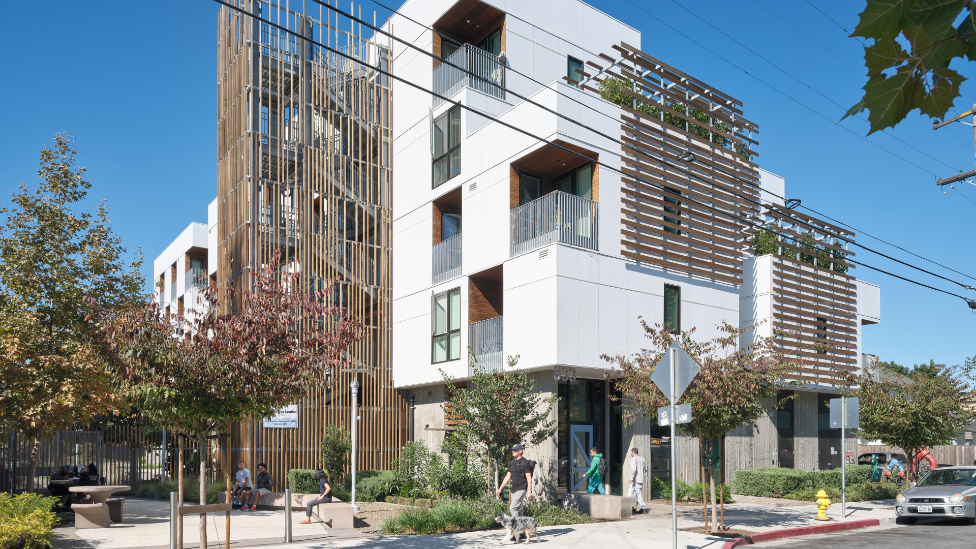 Corner view of white apartment building with wooden stair tower, trellises, and blue front door