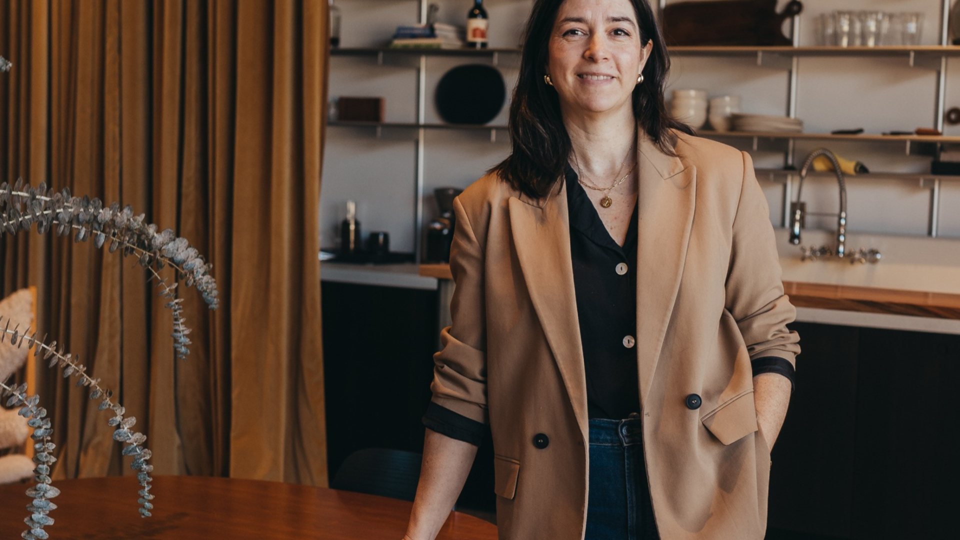 Woman in tan blazer standing beside table