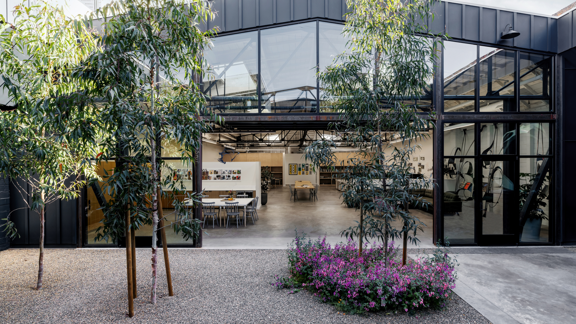 Steel frame building with open garage door and glass and small trees in the foreground courtyard 