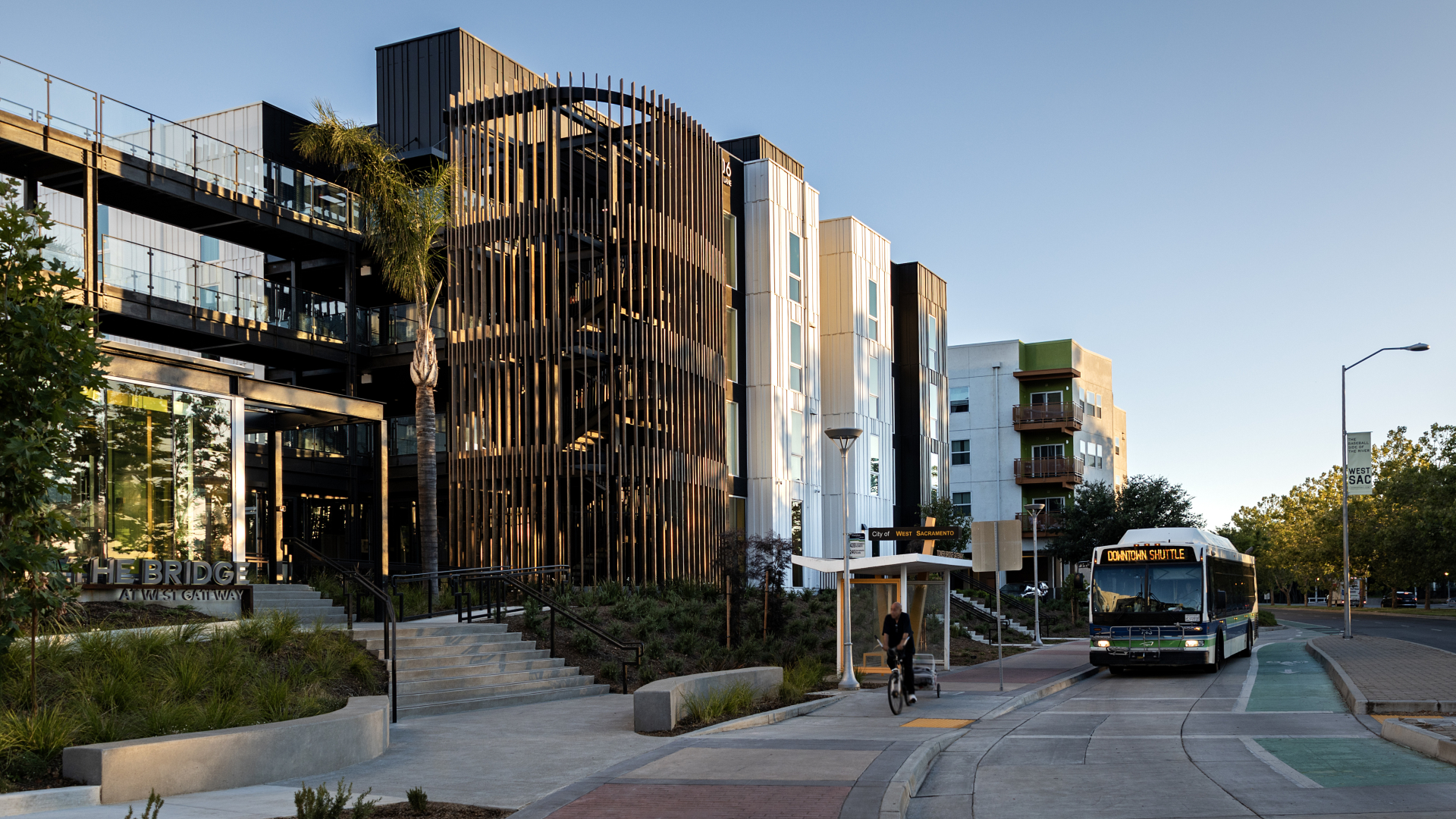 Multifamily building with rounded wood-slatted stair tower, with bus at bus stop in front