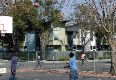 Kids playing basketball at the basketball court with Magnolia Row in West Oakland, California in the background.