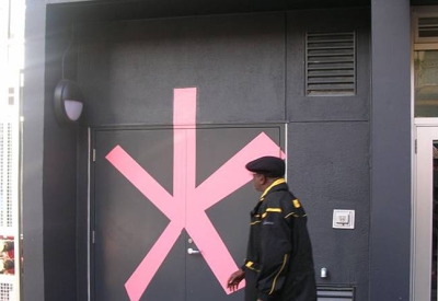 Man waling past a painted mural on the dark facade of Curran House showing a big pink asterisk with a handwritten legend in yellow reading "Incredible but true"