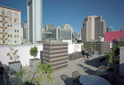 View of seating and small citrus trees in planters ringing the rooftop garden, with city views in background. 