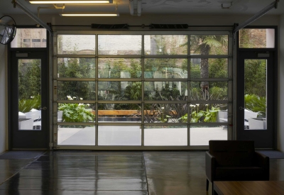 View from the lobby through a glass roll-up garage door into the planted courtyard.