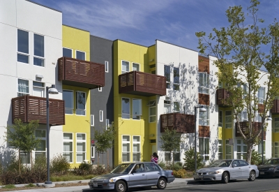 Elevation of apartment building with wood-slat balconies and a planted sidewalk at Tassafaronga Village in East Oakland, CA. 