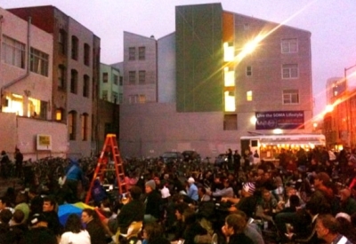Crowd sitting on the ground watching a movie with SOMA Residences in San Francisco in the background.