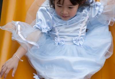 Young girl sliding down the slide in a princess costume at Paseo Senter in San Jose, California.