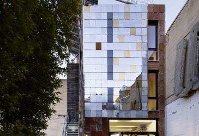 Exterior of Zero Cottage at dusk, with lights on in ground-floor workshop in San Francisco..