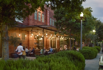 View from the southwest of people sitting at tables at Bettola Patio underneath the trellis at dusk in Birmingham, Alabama.