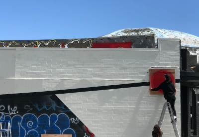 Two people on a ladder outside of David Baker Architects office to put up art on the wall.