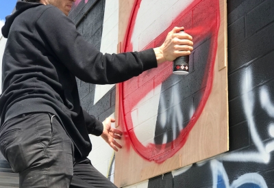 A man spray painting a red circle on the side of David Baker Architects office in Oakland, California.
