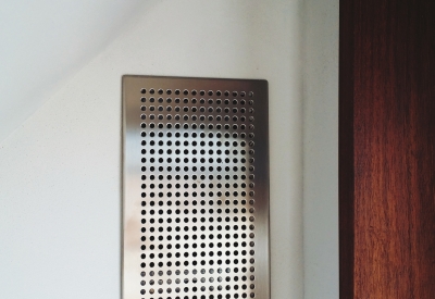 The Heat Recovery Ventilator, a silver vent on the on the wall in Zero Cottage in San Francisco.