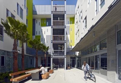 Sunny view of courtyard facing open-air stair tower, with people sitting and walking bikes