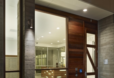 Night view of illuminated glass-front lobby and custom redwood front door at Richardson Apartments