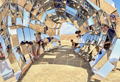 A group of people, the DBA_Lab team poking their heads inside peepSHOW, in the desert in New Cuyama, California.