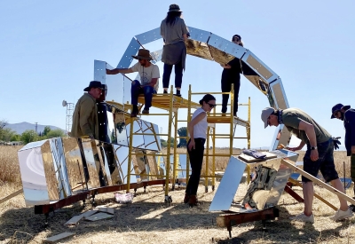 A group of people in building peepSHOW with blue skies in the desert in New Cuyama, California.