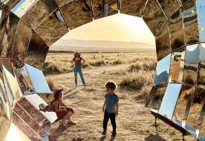 Two children playing inside the reflective peepSHOW in the sun in the desert in New Cuyama, California.