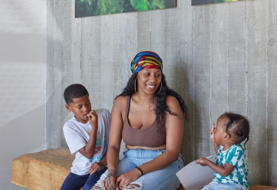 Woman and two children sitting on a bench inside the lobby of Coliseum Place in Oakland, California.