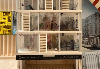Model on display in a plywood pavilion.
