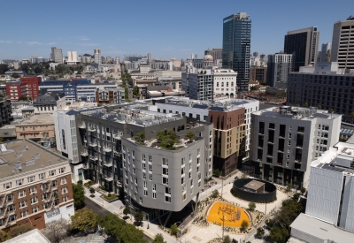 Aerial view of diverse buildings centered around a landscaped urban park with blue sky in background.