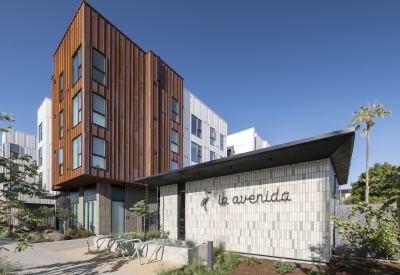 Entry of La Avenida Apartments with heron logo and building signage in cursive on a tiled wall. 