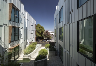 View toward street from narrow podium courtyard with planter boxes and perforated sunshades. 