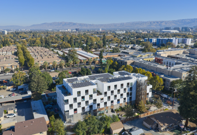 Aerial view of side of white apartment building in cityscape with hills and blue sky in background