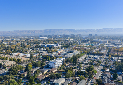 Distant aerial view of white apartment building in cityscape with hills and blue sky in background