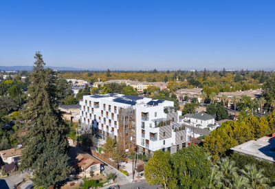 Aerial view of front corner of white apartment building in cityscape with hills and blue sky in background