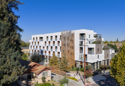 White apartment building with decorative wood stair tower and balconies in a checkerboard pattern