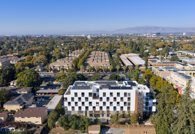 Aerial view of courtyard side of white apartment building in cityscape with hills and blue sky in background