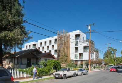 Street level view of white apartment building with wood stair tower next to single family home