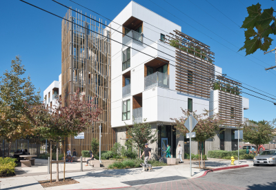 Corner view of white apartment building with wooden stair tower, trellises, and blue front door