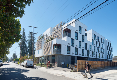 Corner view of white apartment building with wood trellises and driveway entry