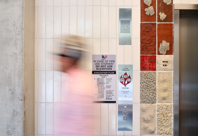 Detail view of white tile wall with textured tile inset and blurry figure waliking past