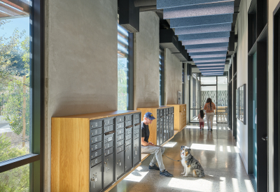 Interior lobby hallway with apartment mailboxes, a man sitting on a bench with a dog, and a woman and child walking in the distance