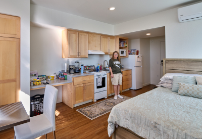 Interior view of studio apartment with woman in green T shirt and shorts posing by the stove