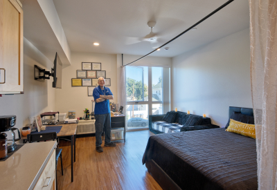 Interior view of studio apartment with man in blue standing with folded arms